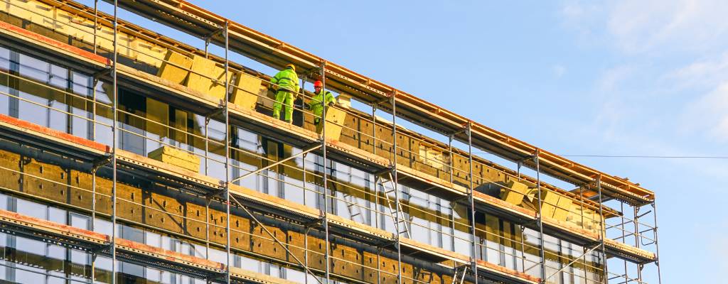 Workers stand on industrial scaffolding as they install thermal insulation on an apartment building.